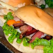Hambúrguer: X-Bacon - Hambúrguer (Ingredientes: Alface, Bacon, Batata Palha, Catupiry, Cheddar, Hambúrguer Aurora, Milho, Molho Especial, Pão, Presunto, Queijo, Tomate)