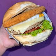 Hambúrguer: X-Steak - Hambúrguer (Ingredientes: Alface, Batata Palha, Catupiry, Cheddar, Hambúrguer Aurora, Milho, Molho Especial, Pão, Presunto, Queijo, Steak, Tomate)