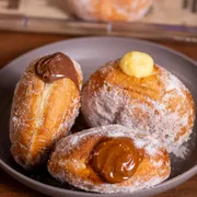 SOBREMESAS: Donuts creme - Nossa exclusiva massa artesanal, fofinha e dourada, recheada com um creme de baunilha super cremoso. Finalizada com aquele toque clássico de açúcar de confeiteiro que derrete na boca.
