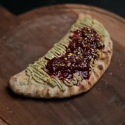 Calzone Doce: Calzone Pistache - Doces (Ingredientes: Massa napolitana assada e recheada com creme de pistache, finalizada com frutas vermelhas e açúcar de confeiteiro, Uma combinação delicada, cremosa e surpreendente)