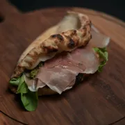 Panuozzo: Panuozzo Parma e Búfala - Panuozzo (Ingredientes: Panuozzo leve e crocante, recheada com presunto parma, queijo de búfala, rúcula fresca e pesto genovese. Uma experiência italiana autêntica, que combina frescor, cremosidade e elegância em cada mordida)