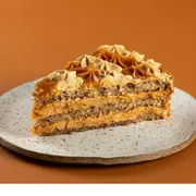 Torta: Fatia de Torta de Churros - Finas camadas de um delicioso pão de ló de canela, com duplo recheio de doce de leite toffee, decorada com doce de leite, mousse de doce de leite e crumble de canela.