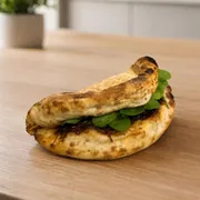 Panuozzo: Panuozzo de Brisket - Panuozzo artesanal inspirado no tradicional street food italiano de Gragnano. Feito com nossa massa de pizza de fermentação natural por 72 horas, assado em forno de pizza e recheado com brisket desfiado, cebola caramelizada, queijo derretido e rúcula fresca. Leve, aerado e cheio de sabor em cada mordida.